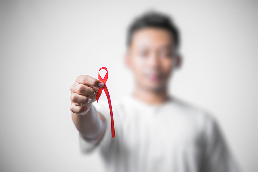 closeup of a young man with a red awareness ribbon for the fight against AIDS in his hand